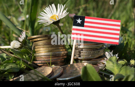 Liberianischer Flagge mit Stapel von Geld Münzen mit Rasen und Blumen Stockfoto