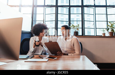 Aufnahme von zwei jungen Unternehmern zusammen am Schreibtisch sitzen. Mann zeigt etwas in Zwischenablage zur Frau im Büro. Stockfoto