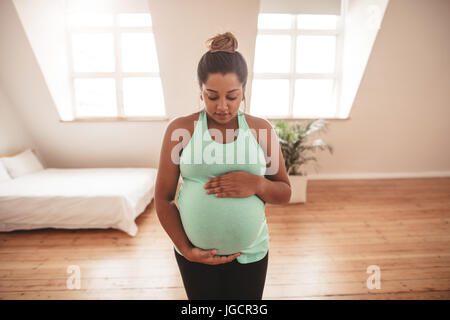 Porträt einer schönen schwangeren Frau, die Yoga-Übungen macht und ihren Bauch berührt. Schwangere Frau, die zu Hause Yoga praktiziert. Stockfoto