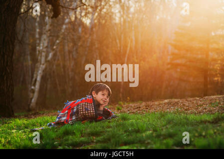 Junge auf dem Rasen, eingewickelt in eine Decke in der Sonne liegen Stockfoto