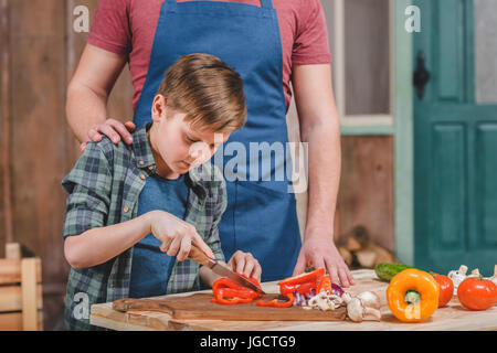 Vater in Schürze hilft Sohn Schneiden von frischem Gemüse im Freien, Vater und Sohn Kochen Konzept Stockfoto