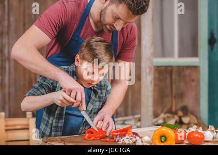 Vater in Schürze hilft Sohn Schneiden von frischem Gemüse im Freien, Vater und Sohn Kochen Konzept Stockfoto