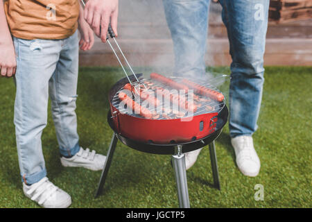 Teilansicht von Vater und Sohn, Hot-Dog Würstchen auf dem Grill kochen Stockfoto