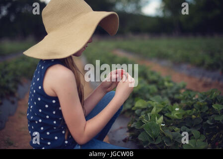 Mädchen sitzen in einem Feld Erdbeeren pflücken Stockfoto