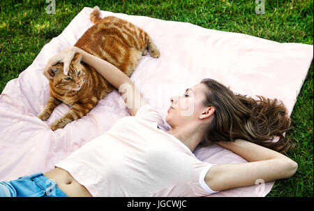 Junge Frau liegend auf einer Decke im Garten ihre Katze streicheln Stockfoto