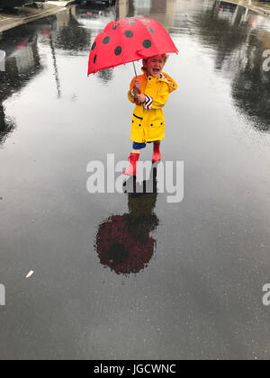 Weinende junge trägt einen Regenmantel und Wellington Stiefel stehen im Regen mit einem Regenschirm, Orange County, California, Amerika, USA Stockfoto