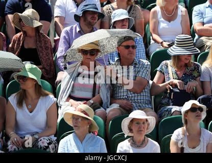 Am dritten Tag der Wimbledon Championships im All England Lawn Tennis and Croquet Club, Wimbledon, schützen sich die Zuschauer unter Sonnenschirmen und Sonnenhüten vor der Sonne. Stockfoto