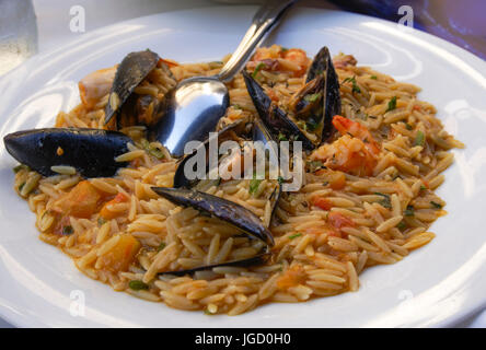 Meeresfrüchte mit gekochten Muscheln in der Schale, Garnelen ohne Schale, Tomaten, Petersilie und Zwiebeln auf einem weißen Teller mit Löffel. Stockfoto