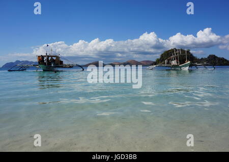 Angelboote/Fischerboote umgewandelt für Touristen.  Low shot Sand, blaues Meer, Boote, Hügel Bereich / Klippen, strahlend blauer Himmel, weiße flauschige Wolken. Coron, Philippinen. Stockfoto