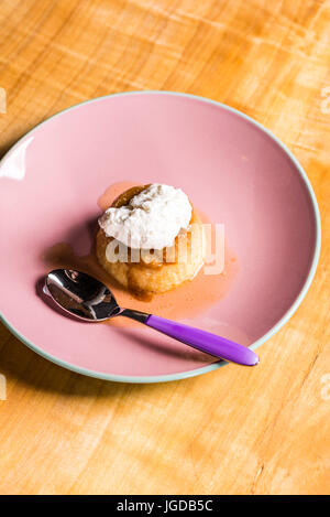 Flan - eine süße Pudding Creme Caramel mit Creme obendrauf, auf einem rosa Teller über ein Holzbrett. Stockfoto