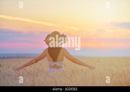 Closeup Portrait von lächelnden jungen kaukasischen Frau in Natur. Freundliche junge schöne Frau berühren Weizenfeld bei Sonnenuntergang Stockfoto