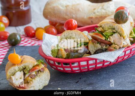 Gehen Sie lassen Sie uns auf ein Picknick! Gourmet-gegrilltes Hähnchen-Sandwiches serviert mit französischen Brötchen, rot karierte Tischdecke und rote Take-out Korb - Yum! Stockfoto