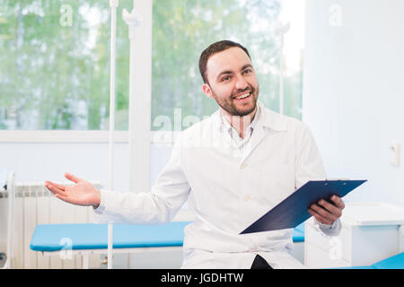 Fröhliche junge Ärztin hält ein Klemmbrett und Gestikulieren mit seiner Hand auf Krankenstation Stockfoto