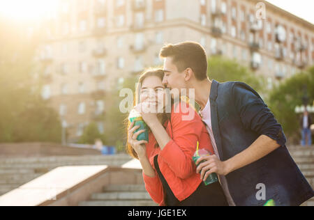 Jugendliche trinken Obst frisch aus Gläsern. Er flüstert zärtlichen Worte in ihr Ohr. Sie lacht kokett. Ein Liebespaar auf ein Datum. Romantik des ersten l Stockfoto