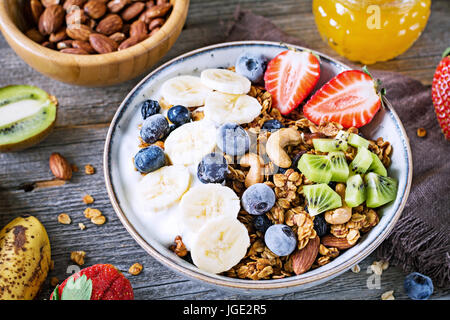 Müsli Schale mit Bananenscheiben, Heidelbeeren, Kiwi und Erdbeeren auf Holztisch, Detailansicht. Gesunde Ernährung, Diät Konzept Stockfoto