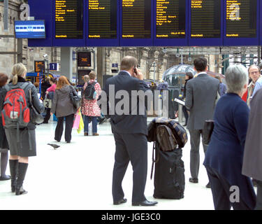 Geschäftsmann auf dem Handy in Glasgow Central Bahnhof vor Anzeigentafel Stockfoto