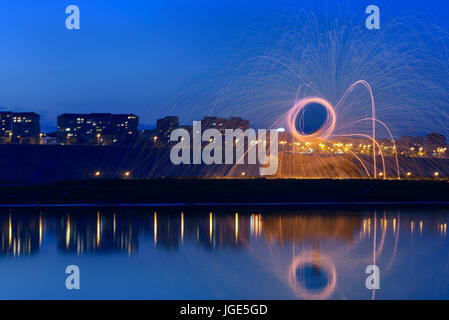 Heiße goldene Funken von man Spinnen brennen Stahlwolle in der Nähe des Flusses mit Wasser Reflexion. Fotos mit langer Belichtungszeit mit Stahlwolle brennen. Stockfoto