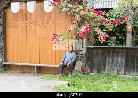 Eine Mann-Pause auf einer Bank auf der Straße in Oncesti, Region Maramures, Rumänien Stockfoto