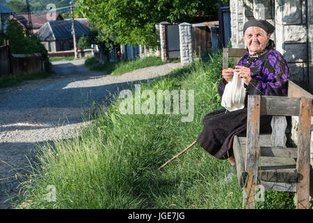 Eine ältere Frau tun häkeln auf einer Bank auf dem Weg zu Oncesti, Region Maramures, Rumänien Stockfoto