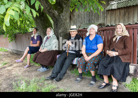 Fünf ältere Leute sitzen auf einer Holzbank auf einer kleinen Landstraße in der Maramures-region Stockfoto
