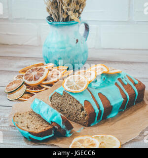 Banane und orange Kuchen mit blauen Glasur und getrockneten Zitrone auf hölzernen Hintergrund und Kraft Papier. Stockfoto