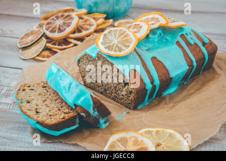 Banane und orange Kuchen mit blauen Glasur und getrockneten Zitrone auf hölzernen Hintergrund und Kraft Papier. Stockfoto