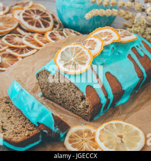 Banane und orange Kuchen mit blauen Glasur und getrockneten Zitrone auf hölzernen Hintergrund und Kraft Papier. Stockfoto