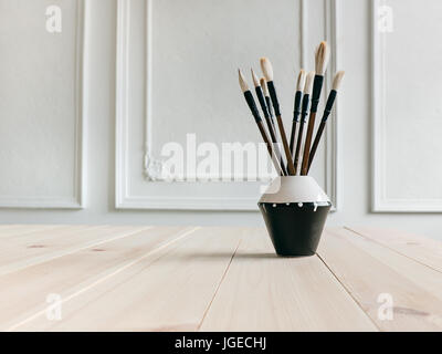 Pinsel auf Schreibtisch verschiedene Pinsel Borsten in einer Keramikvase stehen auf einem Holztisch Fotohintergrund für Text Platz, Textfreiraum Stockfoto