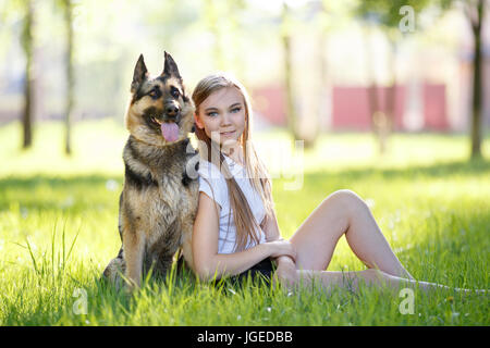 Teenager-Mädchen in weißen Hemd mit ihrem Hund sitzen auf dem Rasen im park Stockfoto