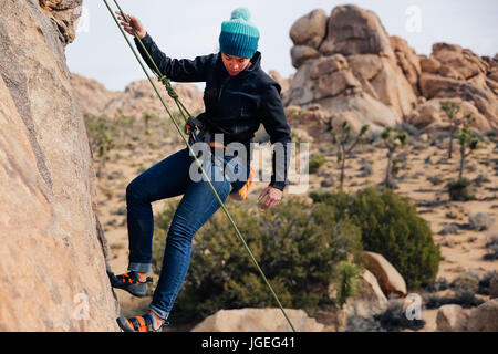 Junge Mischlinge Frau gekleidet für kaltes Wetter Felsen klettert in der Wüste Stockfoto