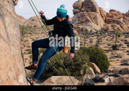 Junge Mischlinge Frau gekleidet für kaltes Wetter Felsen klettert in der Wüste Stockfoto