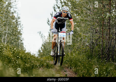 junge männliche Radsportler auf einem Waldweg bei regionalen Wettkämpfen auf Mountainbike Stockfoto