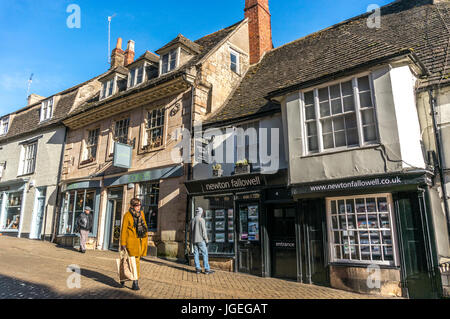 Eine gut gekleidete Frau, lokale Geschäfte und Immobilienmakler in historischen Gebäuden, früh am Morgen ein Winter in Stamford Town, Lincolnshire, England, UK. Stockfoto