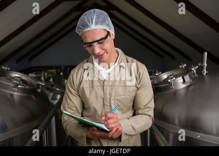 Männliche Arbeiter stehen inmitten von Lagertanks schreiben auf Zwischenablage am Lager Stockfoto