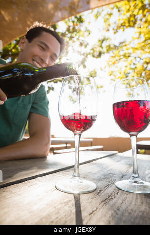 Lächelnden Mann Gießen Rotwein aus der Flasche im Glas am Tisch Stockfoto