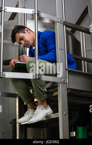 Junge männliche Arbeiter schreiben in Zwischenablage durch Vorratsbehälter auf Lager Stockfoto