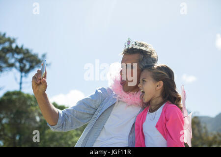 Lächelnd, Vater und Tochter in Fee Kostüm nehmen Selfie auf Handy im Garten Stockfoto