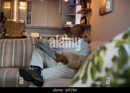 Ältere Mann liest Zeitung beim Sitzen auf dem Sofa zu Hause Stockfoto