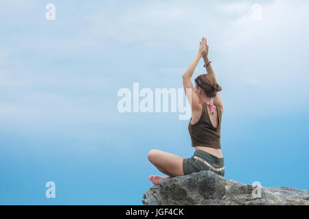 Mädchen üben Yoga Meditation auf einem Felsen am blauen Himmelshintergrund. Entspannung und Dehnung. Stockfoto