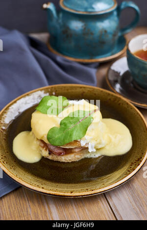 Frühstück. Leckeren Eiern Benedict auf Teller serviert. Teekanne und Tasse heißen schwarzen Tee. Stockfoto