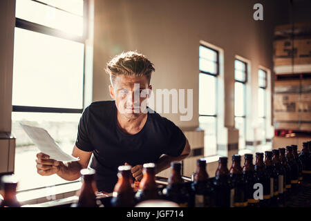 Brauerei Fabrikarbeiter untersucht die Qualität des Craft Beer. Junger Mann Inspektor arbeitet an Alkohol Herstellungsfabrik überprüfen die Bierflaschen. Stockfoto