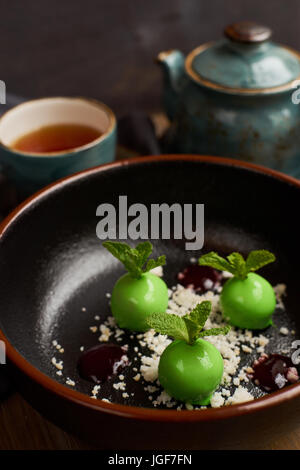 Kochs Dessert aus Äpfeln, Schokolade, Minze und Karamel glasiert in Form von kleinen Äpfel mit Blättern. Mit Teekanne und Tasse heißen schwarzen Tee serviert. Stockfoto