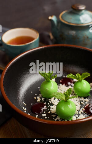 Kochs Dessert aus Äpfeln, Schokolade, Minze und Karamel glasiert in Form von kleinen Äpfel mit Blättern. Mit Teekanne und Tasse heißen schwarzen Tee serviert. Stockfoto