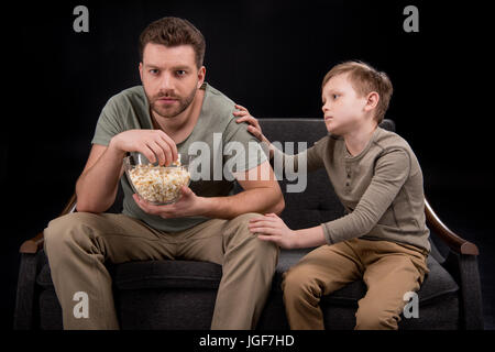 Kleiner Junge versucht, mit Vater Essen Popcorn und vor dem Fernseher auf Sofa, Familienprobleme Konzept reden Stockfoto