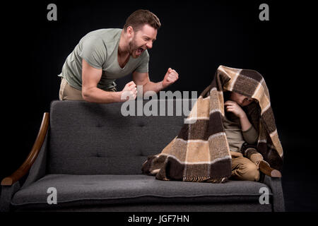 Wütende Vater droht, Angst kleiner Junge versteckt unter der Decke auf Sofa, Familienprobleme Konzept Stockfoto