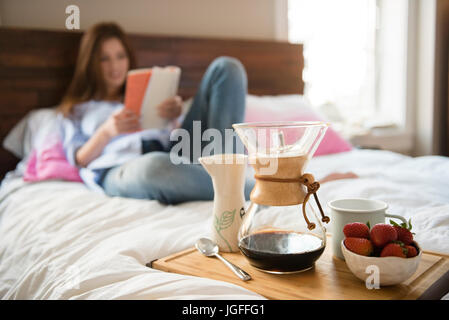 Kaukasische Frau im Bett lesen Buch in der Nähe von Frühstückstablett Stockfoto