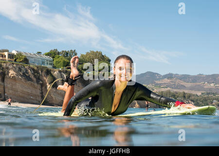 Lächelnde Frau kaukasischen Paddeln auf Surfbrett im Ozean Stockfoto