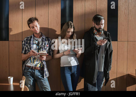 Freunde stehen in der Nähe der Wand mit Gadgets in ihren Händen. Stockfoto