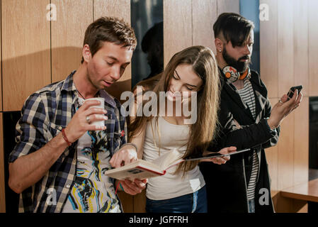 Drei junge Menschen im Raum. Menschen stehen in der Nähe der Wand mit Gadgets in ihren Händen. Stockfoto