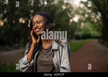 Lächelte attraktive schwarze Mädchen am Telefon im Park. Stockfoto